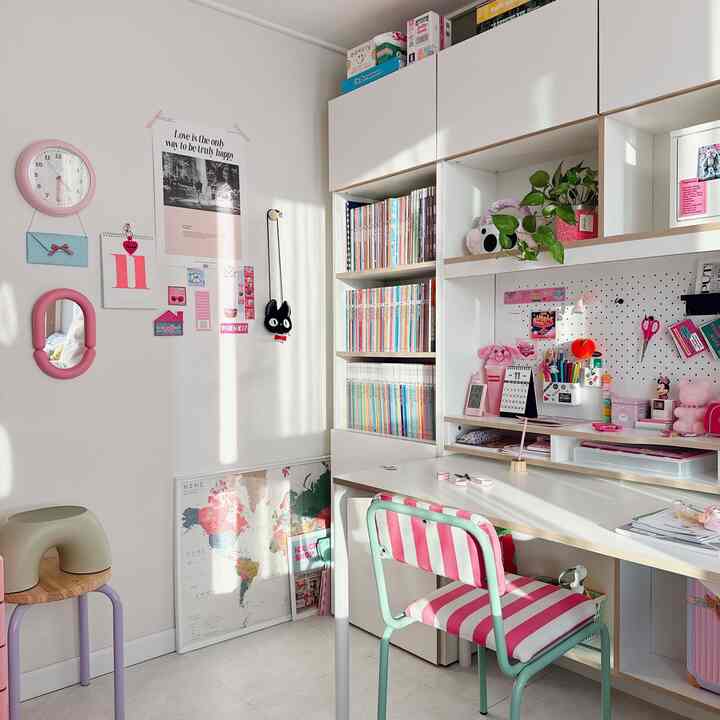 白とピンクのトーンの子供部屋、デスクとピンクのストライプチェアが配置され、壁にポスターと時計が飾られた雰囲気のあるインテリア