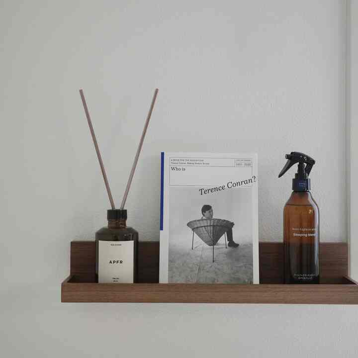 ナチュラルカラーの寝室の壁に無印良品の棚が設置され、ディフューザーや本が配置された印象的な空間