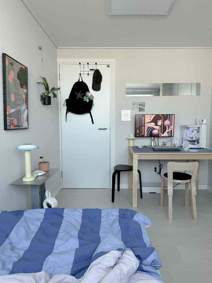 Light gray and natural wood tone bedroom and home office, featuring a simple Nordic-style desk and wall posters in a cozy space