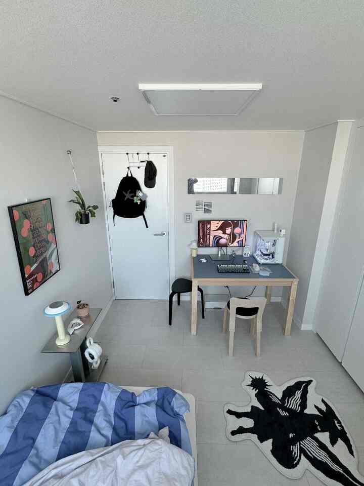 A small bedroom in white and gray tones featuring a mid-century modern desk and poster with a clean atmosphere