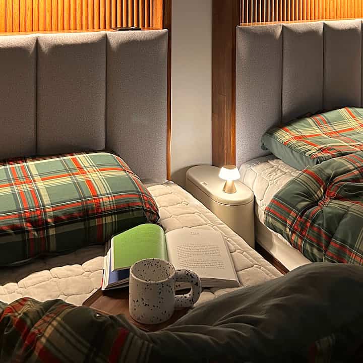 緑のチェック柄寝具と自然な木目調の壁が調和した、暖かく雰囲気のある寝室。小さなテーブルランプが居心地の良さを演出。