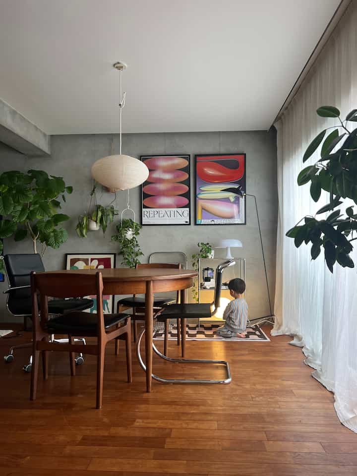 Mid-century modern living room with wood tone flooring and gray walls, featuring posters, plants, and dining table with chairs in a cozy setting