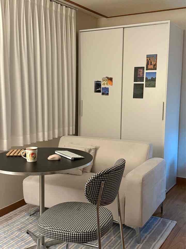 白と黒のトーンが調和したリビング、コンパクトなソファとラウンドテーブルが配置された落ち着いたホームオフィス風インテリア