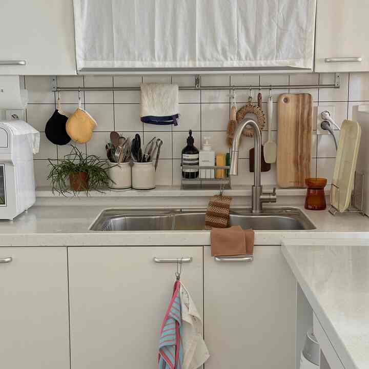 白とナチュラルカラーの小さなキッチン、シンクとカトラリー入れ、タオルが配置された実用的な空間