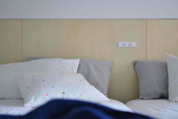 ナチュラルカラーの寝室、白とグレーの枕が配置されたシンプルで落ち着いた雰囲気のインテリア