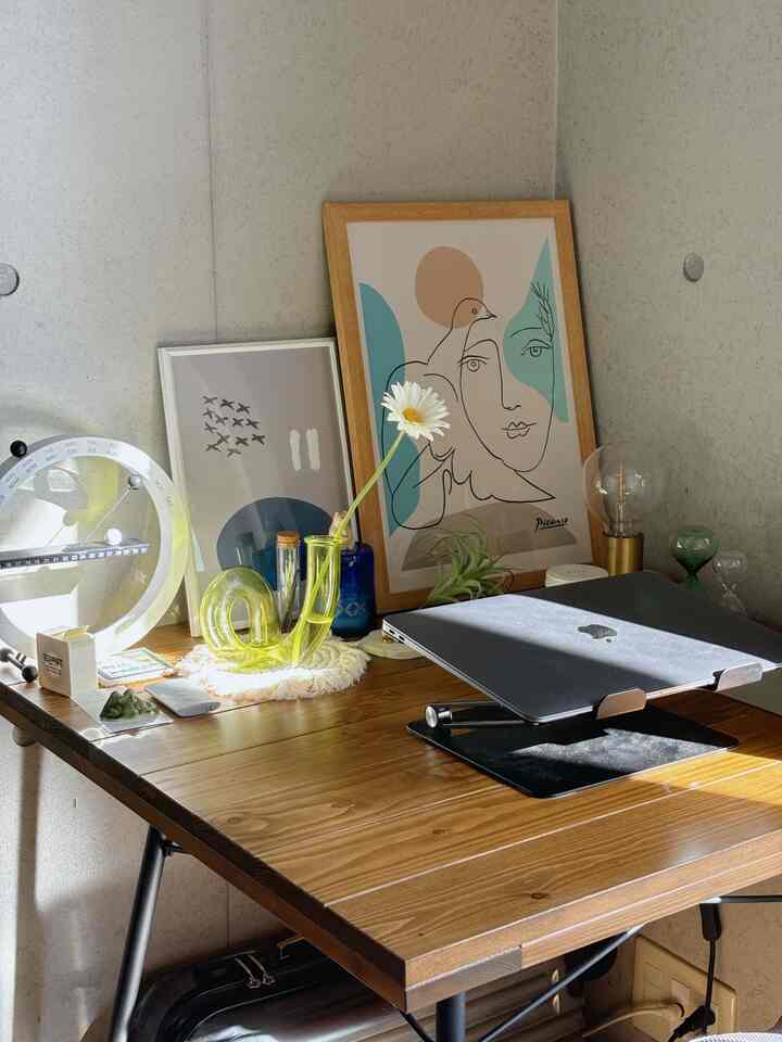 Natural color and wood-tone bedroom corner featuring a desk with a laptop, vase, and framed artwork, creating a cozy atmosphere.