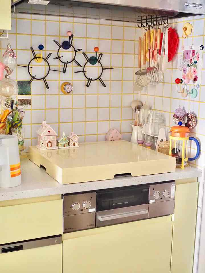 Yellow-tiled wall kitchen featuring yellow cabinets and stove cover, neatly organized kitchen utensils and decorative items