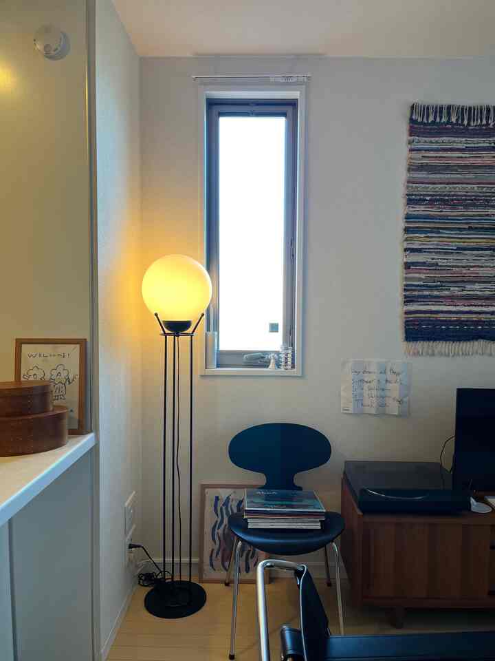 Bright living room with white walls, wood-tone floor, black Ant chair, and glowing floor lamp