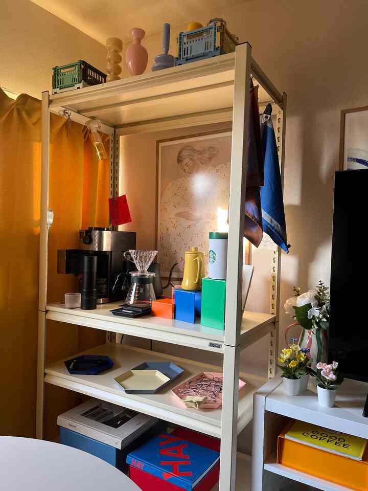 黄色いカーテンと白いスチール棚にコーヒー器具とトレイが配置された、温かみのある落ち着いたおうちカフェの空間