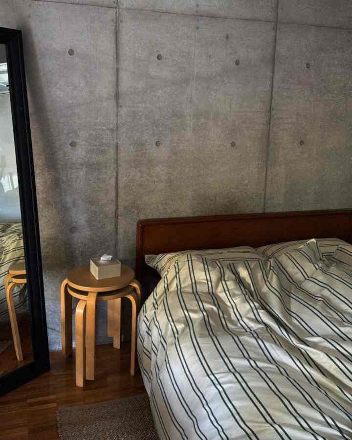 Mid-century modern bedroom featuring concrete walls and wood-tone furniture with striped bedding
