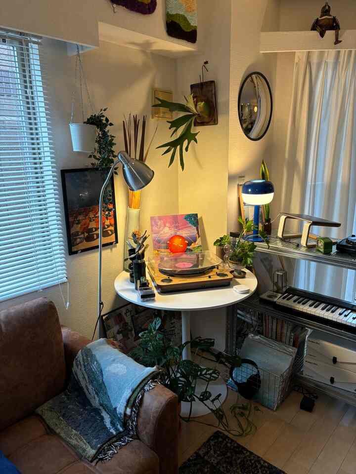 白と茶色のトーンの小さなリビング、レコードプレーヤーが置かれたテーブルとフロアランプ、植物が調和する雰囲気のあるインテリア