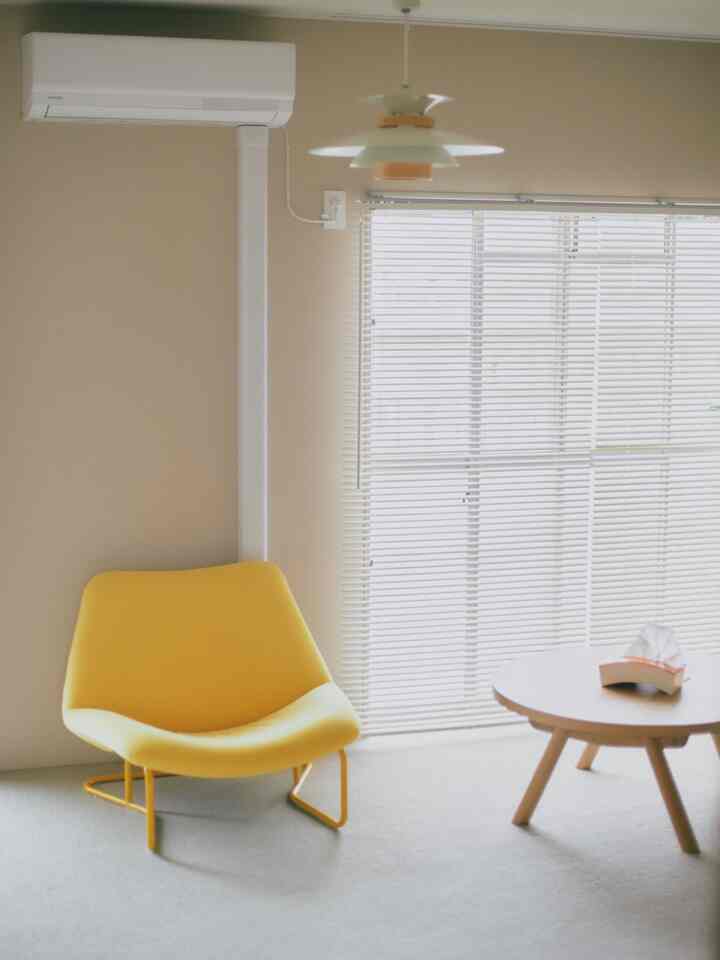 Natural color walls and white blinds in a simple living room, featuring a yellow armchair and wooden round table