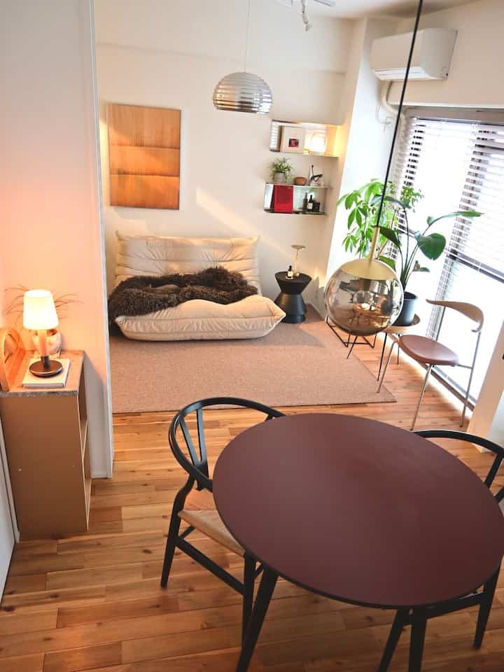 Modern natural living room with white walls and brown wooden floor, featuring a round dining table, sofa, and plants in a cozy setting