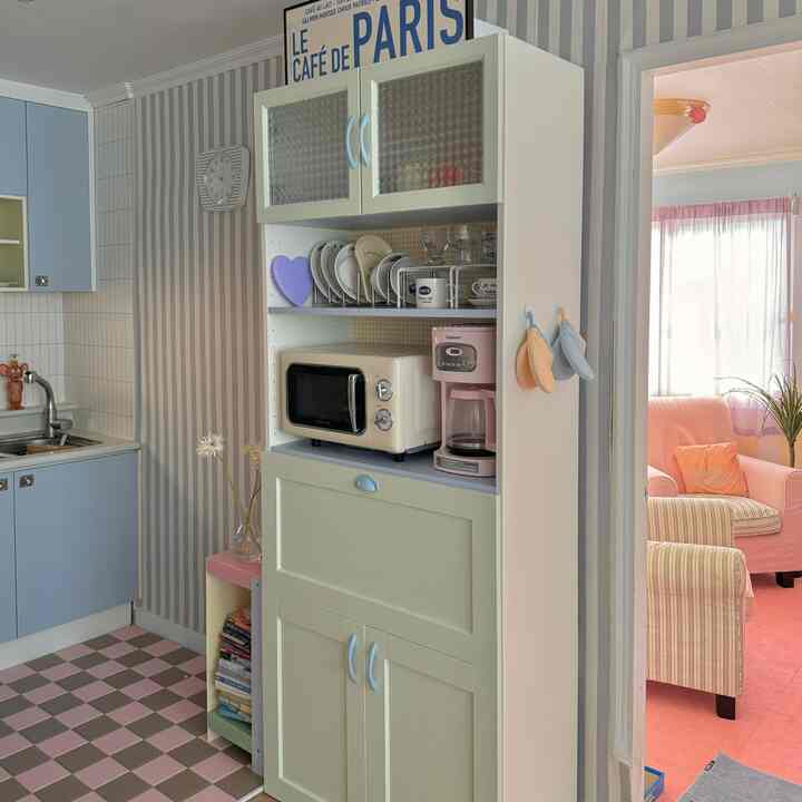 パステル調のキッチンスペース、リフォームされた高さのあるキャビネットが中心にあり、ピンクとスカイブルーの要素が調和した雰囲気のあるインテリア