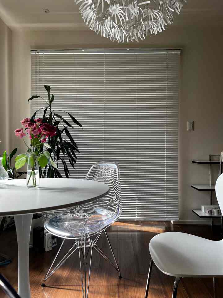 白と木目調が調和するコンパクトなリビング、クリアチェアとブラインドが印象的なカフェ風インテリア