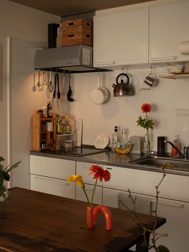 白と茶色のトーンのワンルームキッチン、ユニークな花瓶と花が置かれたシンプルで温かみのあるインテリア