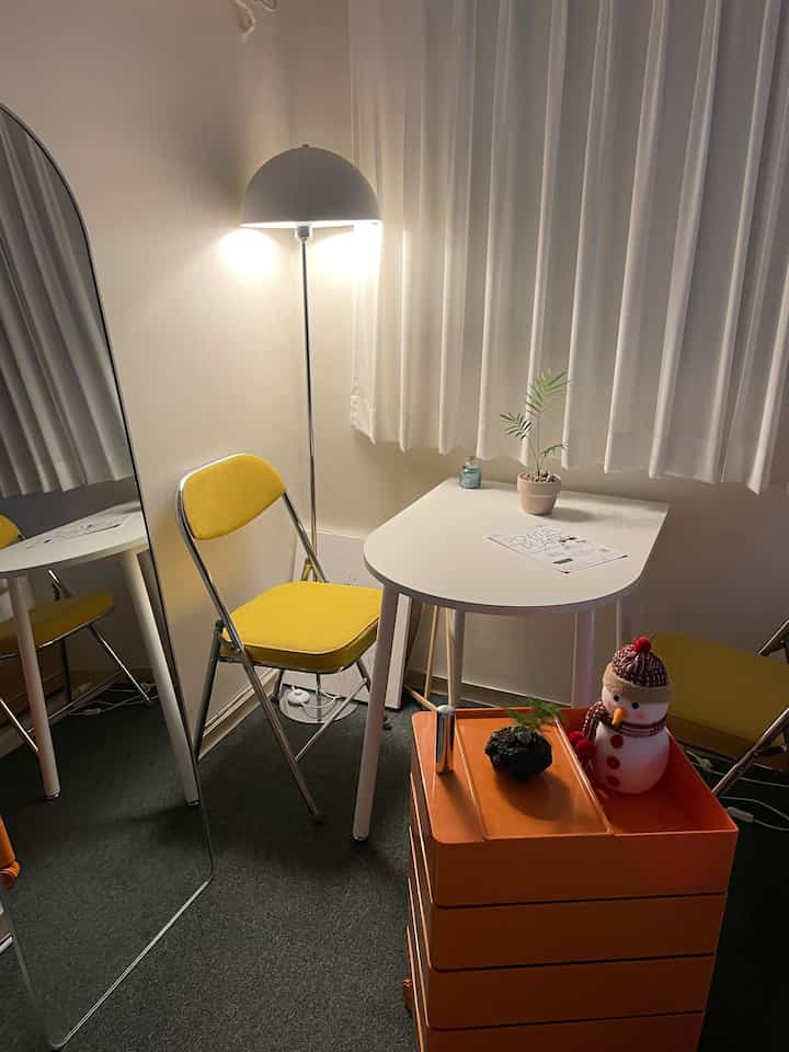 ホワイトとオレンジのトーンのワンルーム、ミニマルな黄色い椅子と白いダイニングテーブルが配置された落ち着いた雰囲気のインテリア