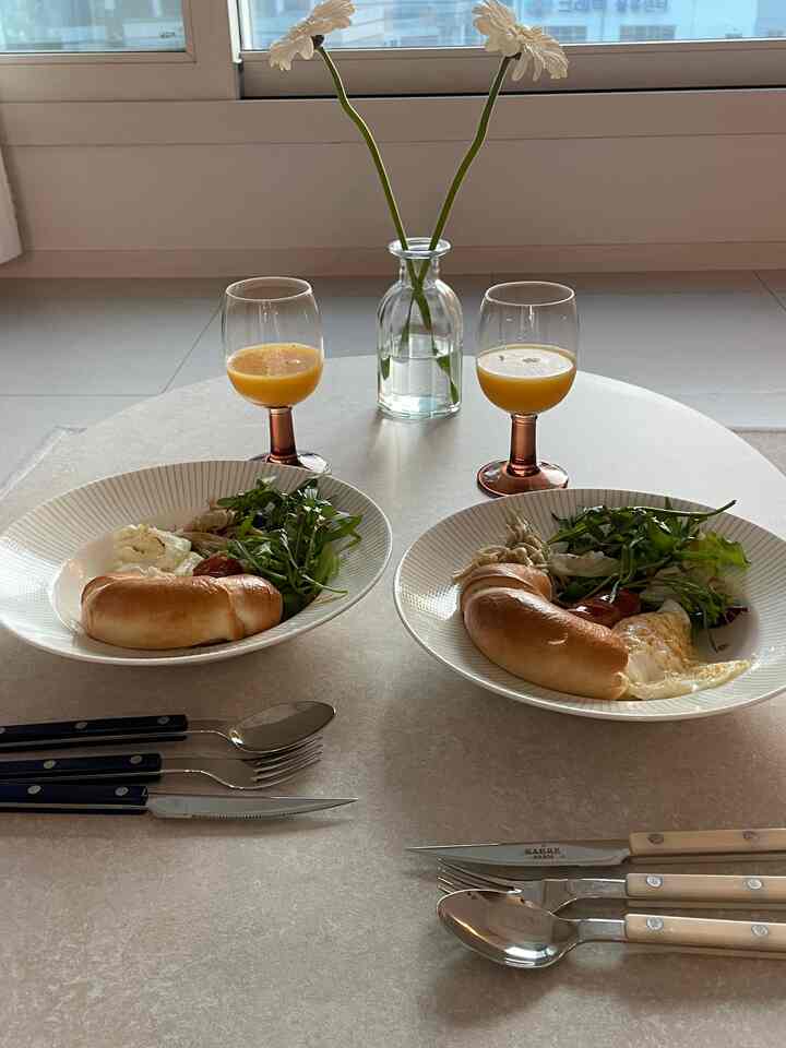 明るいホワイトトーンのダイニングテーブルに置かれた2人分のブランチメニューとカトラリーセット、シンプルでモダンな雰囲気のインテリア