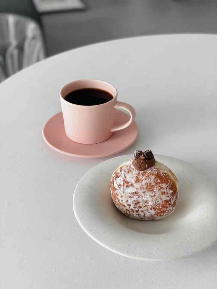 ホワイトトーンのテーブルの上にピンクのカップと白い皿にのったデザートがあるミニマルなホームカフェ空間
