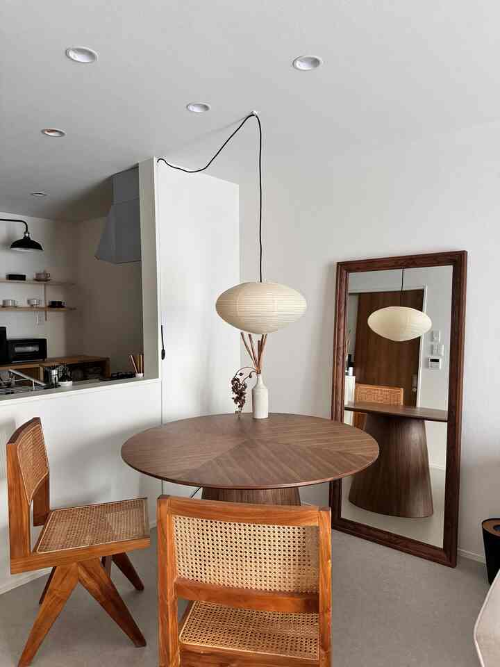 A modern dining room with natural wood tones and beige walls, featuring rattan dining chairs and a round wooden table