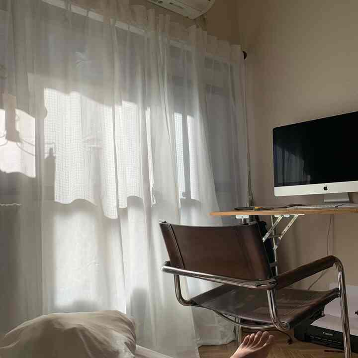 白を基調とした寝室、透ける白いカーテンとシンプルなデスク、ブラウンのオフィスチェアが配置された落ち着いた雰囲気のインテリア