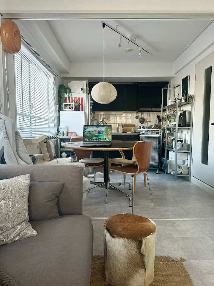 A white and gray toned compact dining room featuring a wooden dining table and chairs, paper pendant light, and sofa with a natural atmosphere.