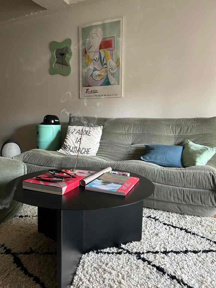 Soft green-toned living room featuring a corduroy sofa and round black coffee table in a cozy space
