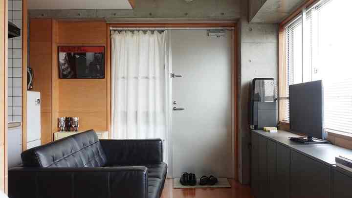 Modern living room featuring a black leather sofa, gray concrete walls, and large windows creating a spacious atmosphere