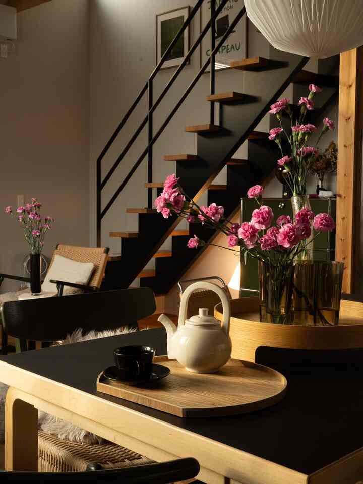 Natural wood tone and black accent living room featuring pink carnations and a teapot on the table with a cozy, modern atmosphere