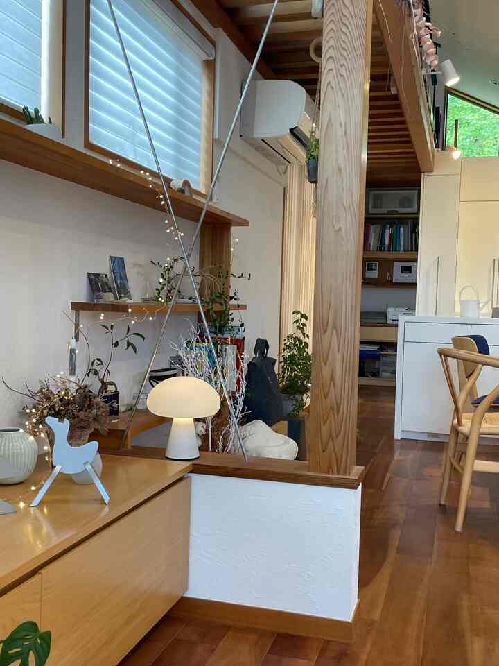 温かみのある木目調とナチュラルな植物が調和したリビング、テーブルランプとウィッシュボーンチェアが配置された落ち着いた空間