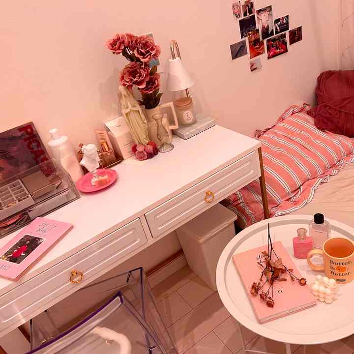 ピンク色の壁とベッド、白いドレッサーと丸いサイドテーブルが配置された居心地の良い一人暮らしの寝室