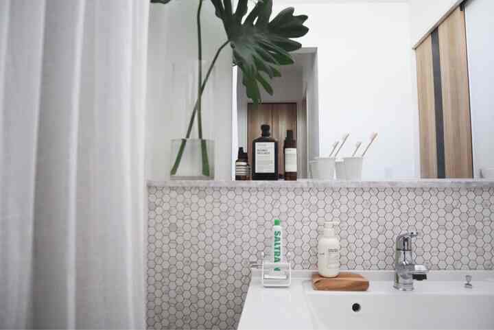 白とナチュラルカラーが調和したバスルーム、洗面台とアロマティックルームスプレーが配置された清潔感のある空間