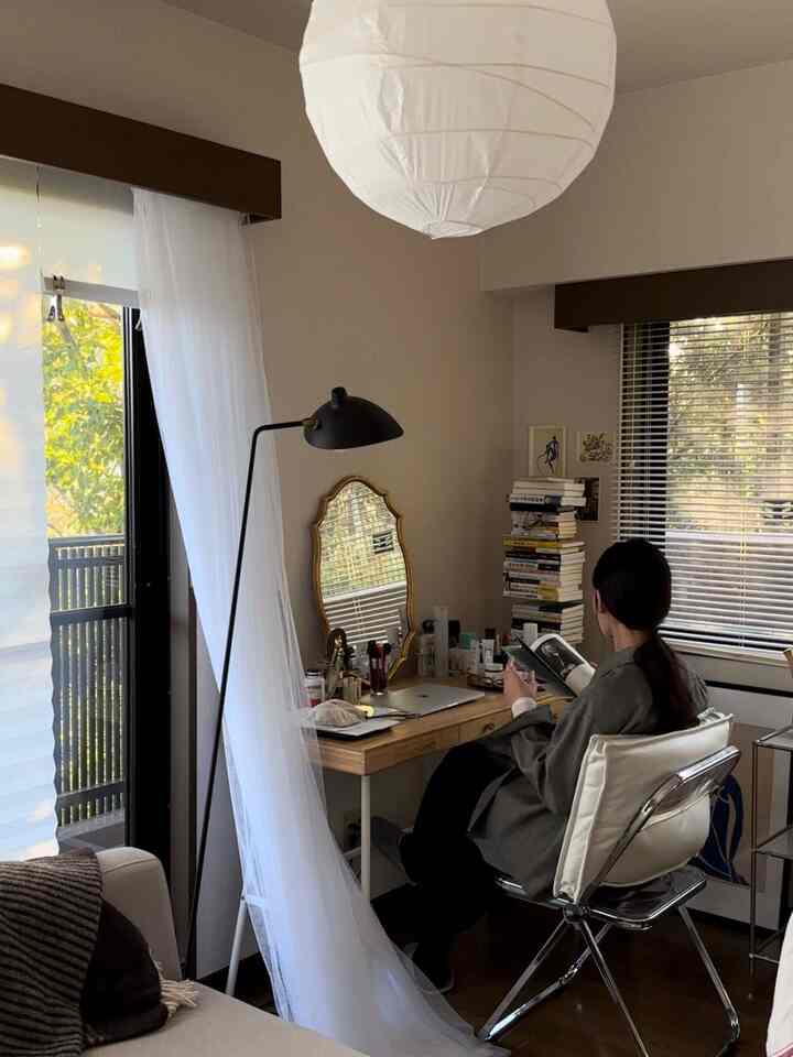 白と茶色の色調があるリビング、自然光が入る窓辺に置かれた机と椅子に人が座って本を読んでいる雰囲気のあるインテリア