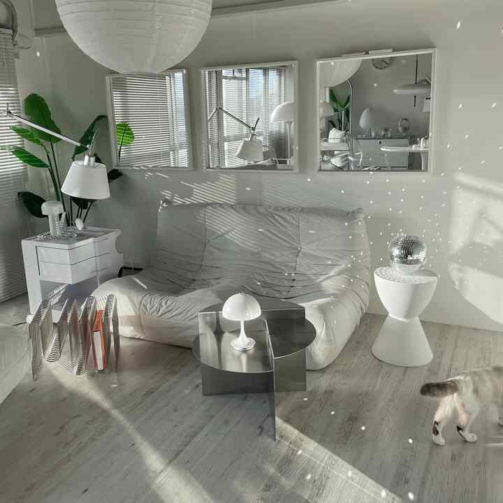 Bright white and natural wood toned living room featuring white sofa, stool, large mirrors, and bamboo plant in a sleek minimal space