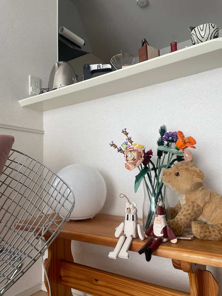 ナチュラルカラーと木目調の小さな卓上に花束と人形が置かれた温かみのある空間