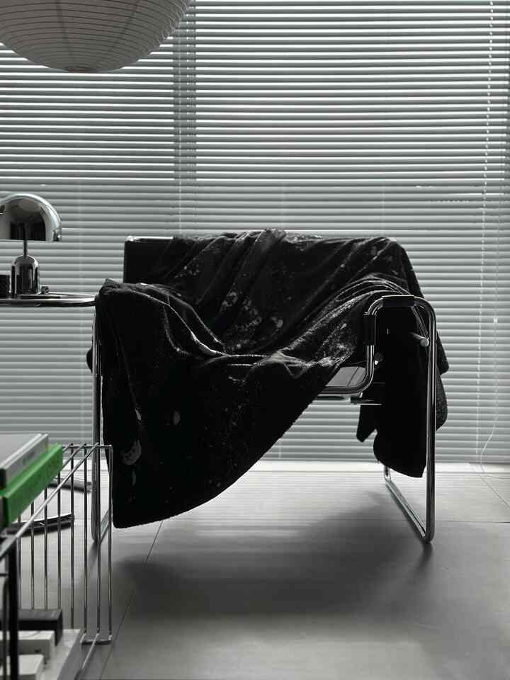 Gray and black toned living room featuring a modern armchair, blinds, and side table with a minimalist atmosphere
