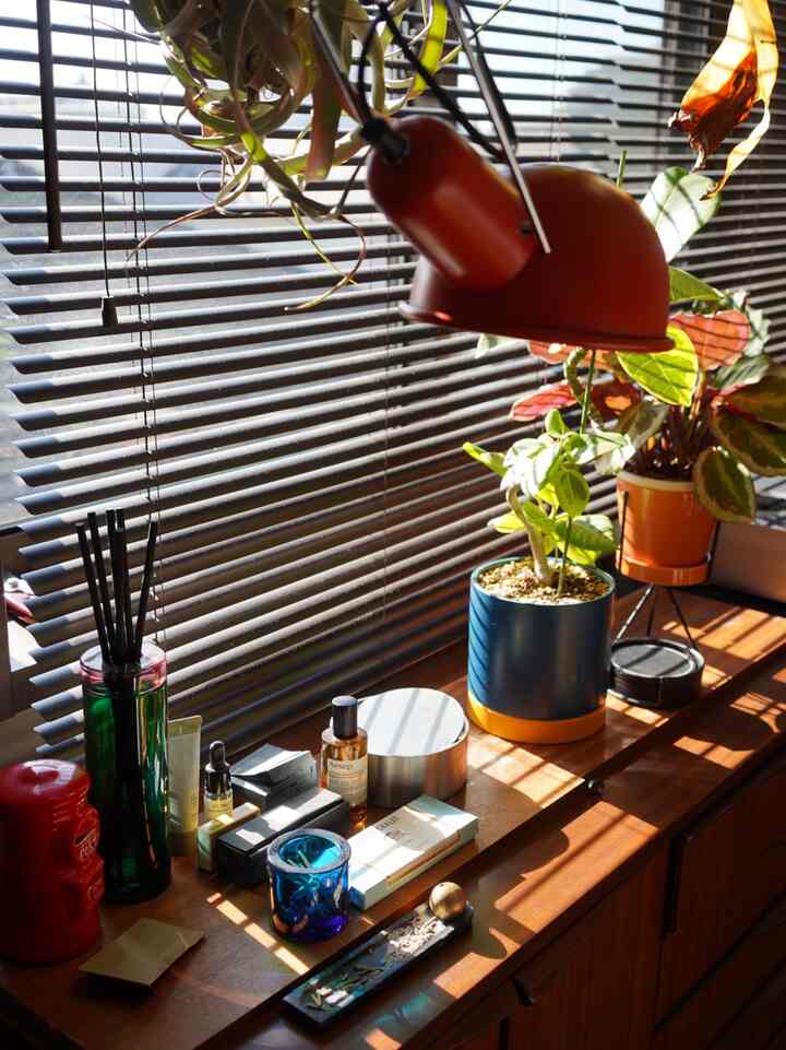 ナチュラルな木目調の窓際キャビネットに植物やディフューザー、赤いテーブルランプが配された温かみのある雰囲気のリビングインテリア