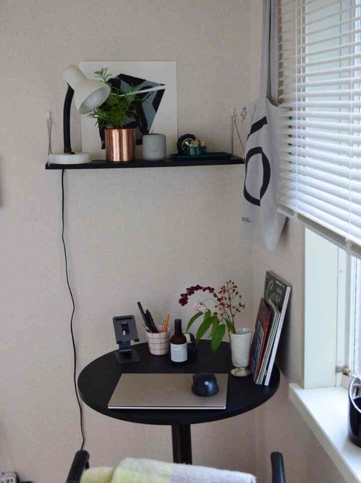 グレーの壁とブラックの丸テーブルが配置されたコンパクトなホームオフィス、植物と照明が雰囲気を演出する居心地の良い空間
