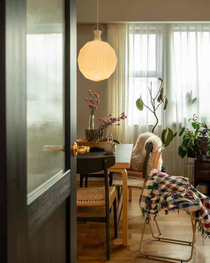 ナチュラルカラーと木目調が調和した北欧風のリビング・ダイニング、木製のテーブルと椅子、植物や明るいカーテンが配置された雰囲気のある空間