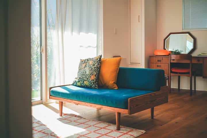 ナチュラルカラーの木目調フローリングと家具が調和したリビング、ターコイズのソファに花柄クッションが置かれた印象的な空間