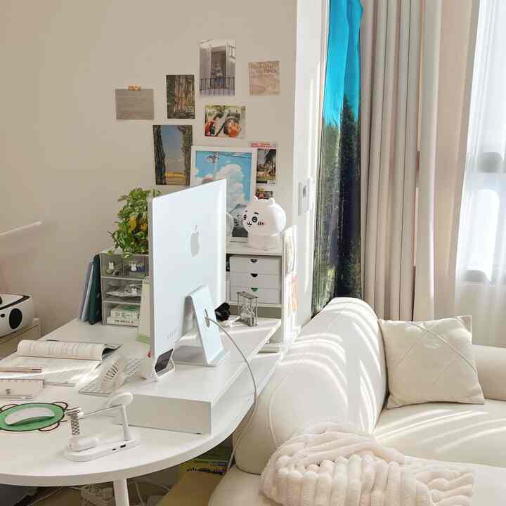 白とベージュのトーンのワンルーム、白いソファとデスク、ポスターが配置された雰囲気のあるホームオフィス空間