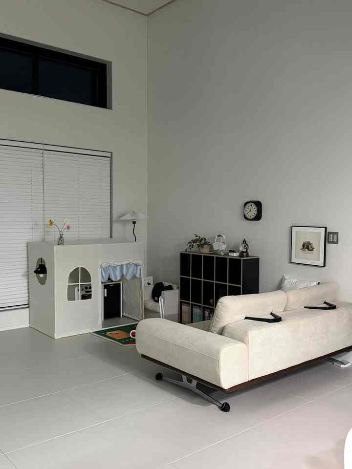 白とナチュラルな木目調が調和した赤ちゃんと暮らすシンプルモダンなリビング、プレイハウスと本棚が配置された居心地の良い空間