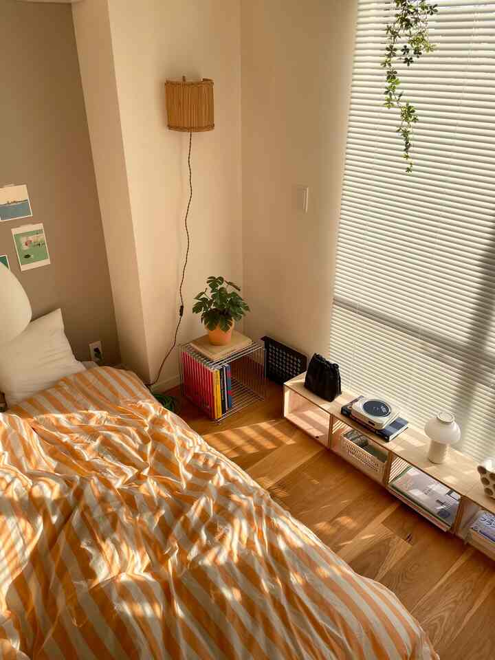暖かみのある木目調と白い壁の寝室、オレンジのストライプの掛け布団と植物が置かれた雰囲気のある空間