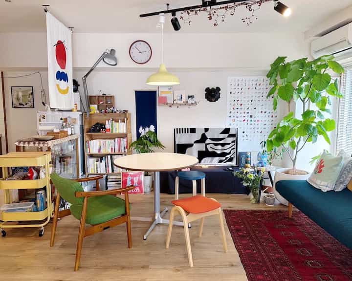 Bright living room with white walls and wood-tone flooring, featuring a green armchair and colorful sofa in a cozy Nordic style