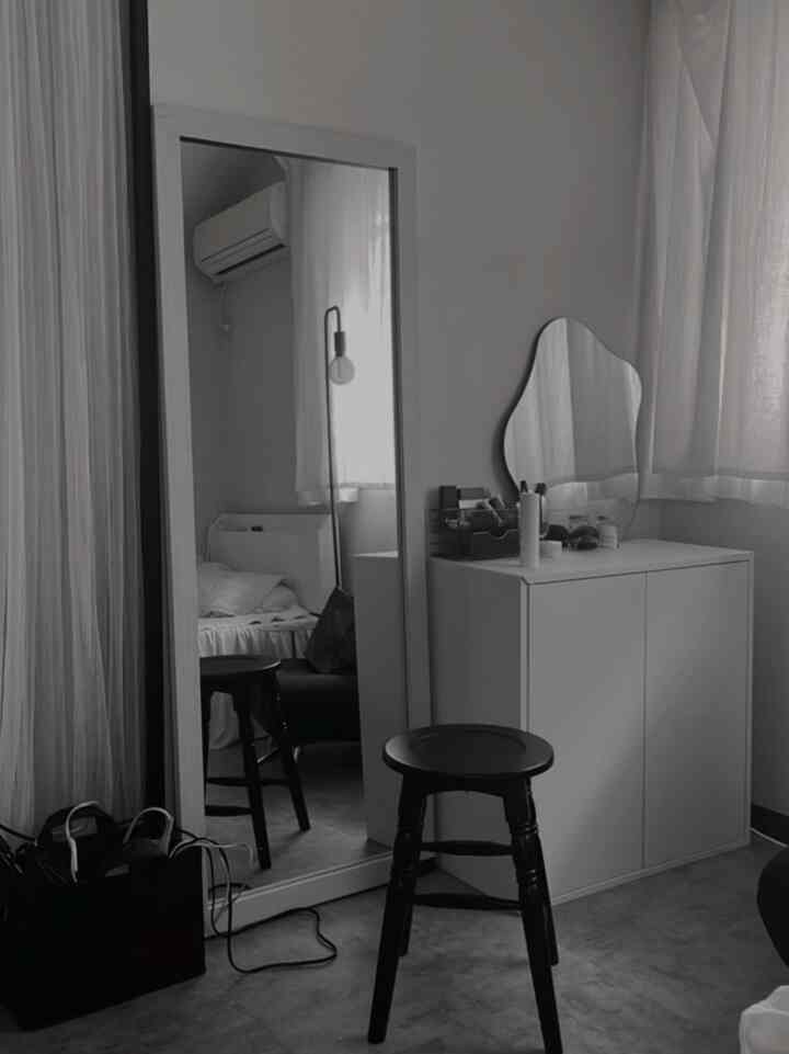 モノトーンの寝室空間、大きな全身鏡と黒いスツール、白いキャビネットが配置されたシンプルでミニマルなインテリア