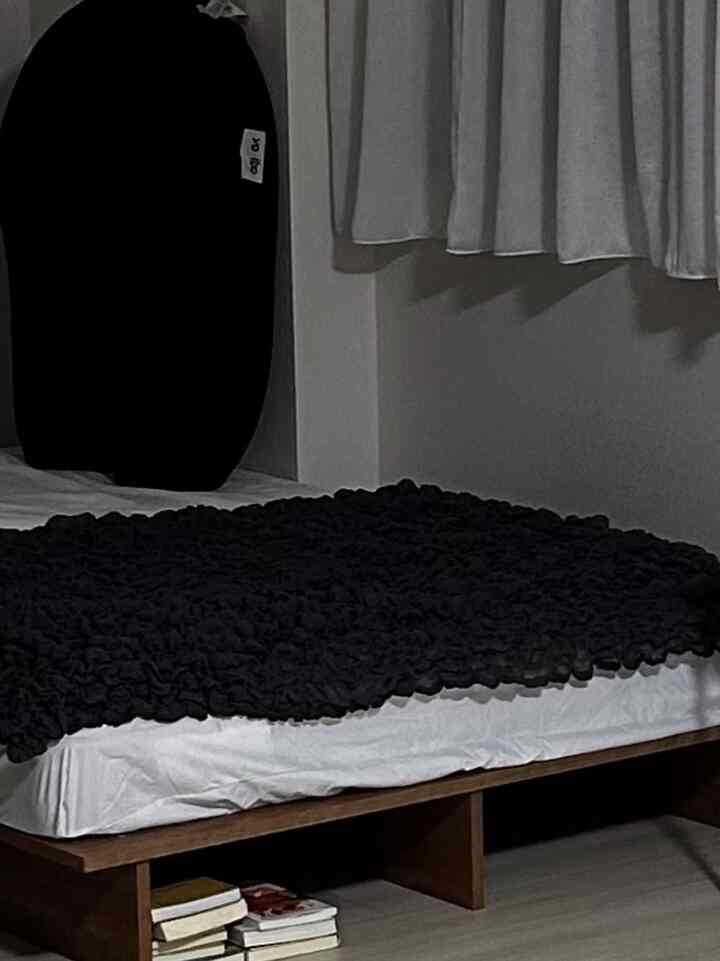 白い寝具と黒いブランケットが敷かれた寝室、黒のビーズクッションが配置された落ち着いた空間