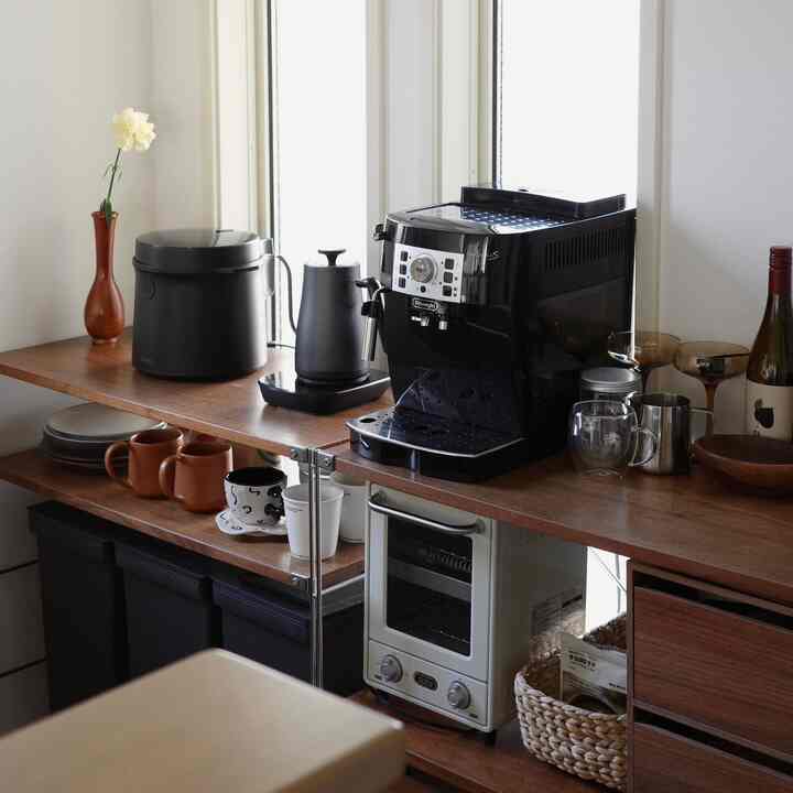 木目調のカウンターに黒いコーヒーマシンと調理器具が置かれたシンプルでモダンなキッチン空間