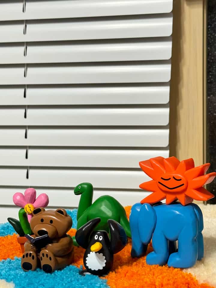 オレンジ色、青色、緑色の玩具フィギュアが配置された、鮮やかなオレンジと青のラグの上の可愛らしいオブジェのあるインテリア