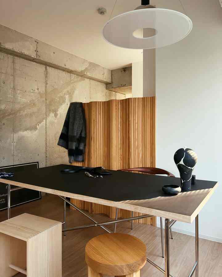 Natural toned dining room featuring a black top dining table, wooden stools, and wooden panel divider with a modern warm atmosphere