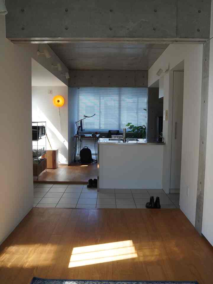 白い壁とナチュラルな木床が調和したワンルームのキッチンとホームオフィスが配置されたモダンな空間